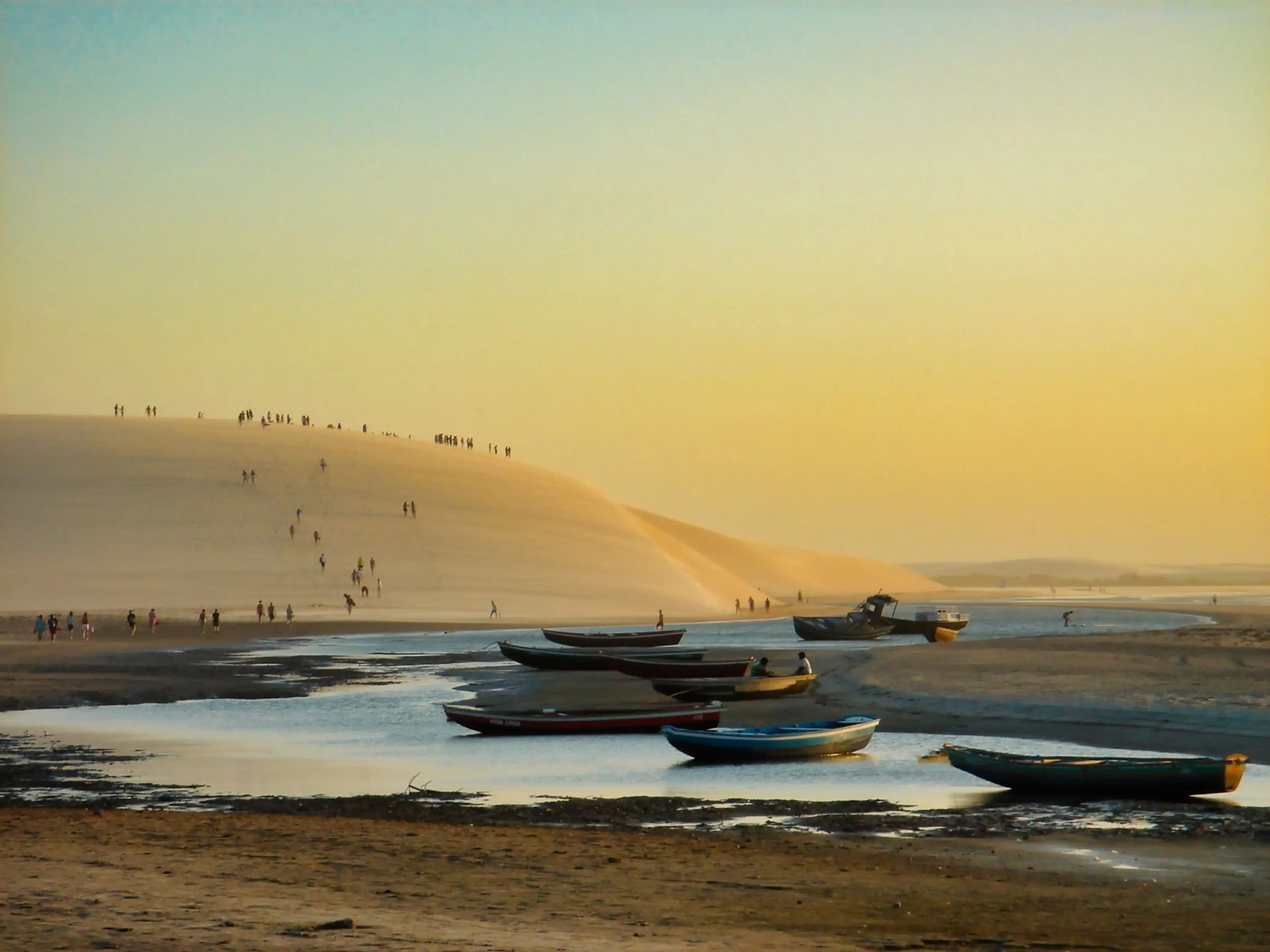 Barcos diante de uma grande duna durante o pôr do sol em Jericoacoara
